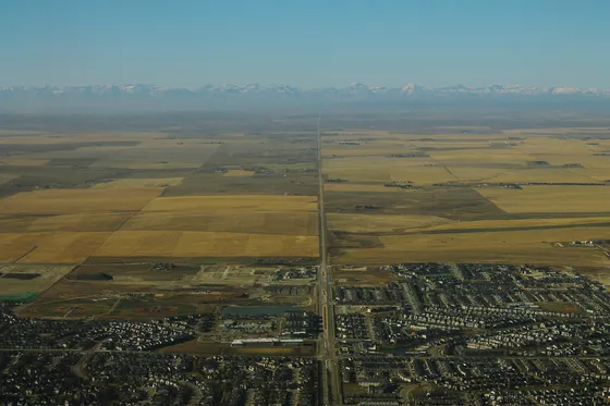Aerial view over houses in Airdrie, Alberta, looking west across farmland to the Rocky Mountains.