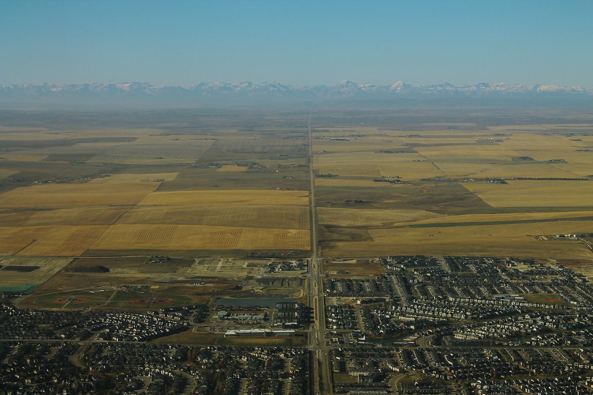 Aerial view over houses in Airdrie, Alberta, looking west across farmland to the Rocky Mountains.